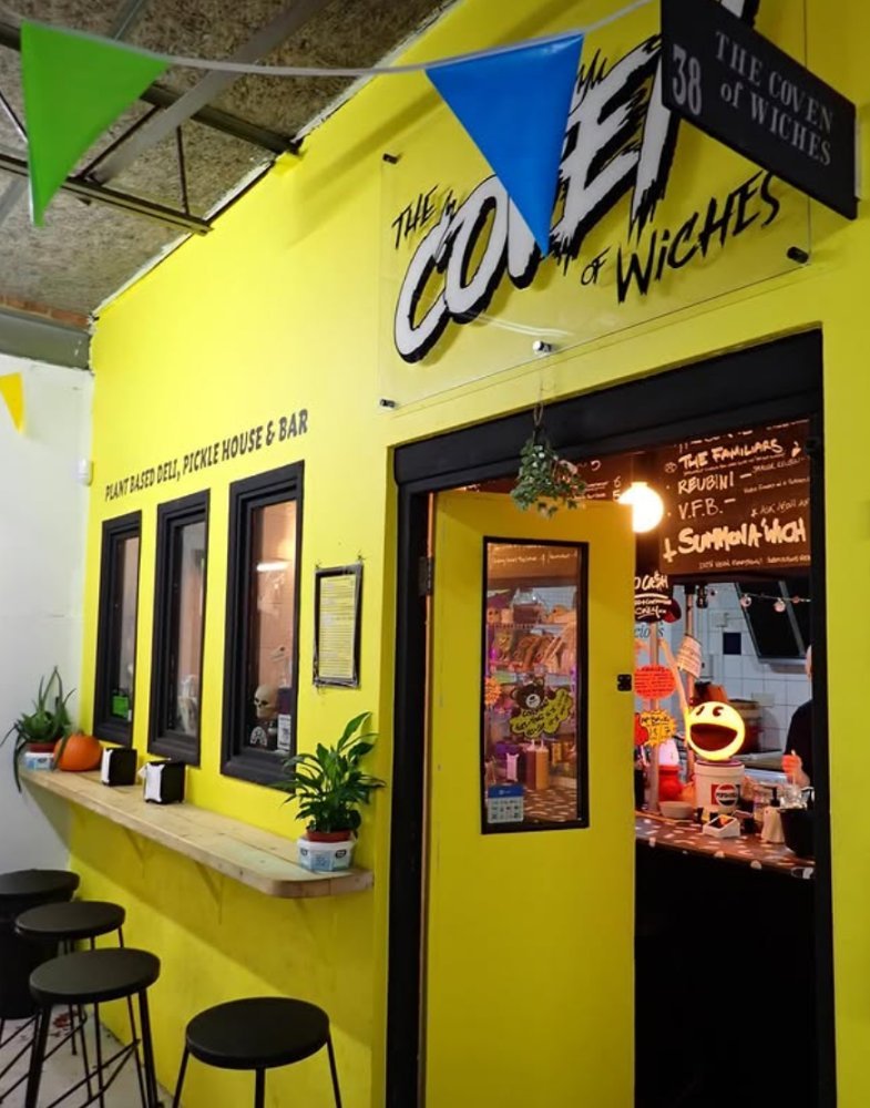 The Coven of Wiches at unit 38, a plant based deli and pickle house with a bright yellow shopfront and bunting overhead