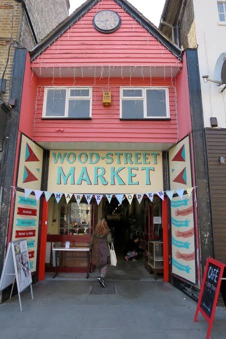 The Wood Street Market entrance, a red shopfront with a clock above the hand-painted market sign and bunting across the doorway