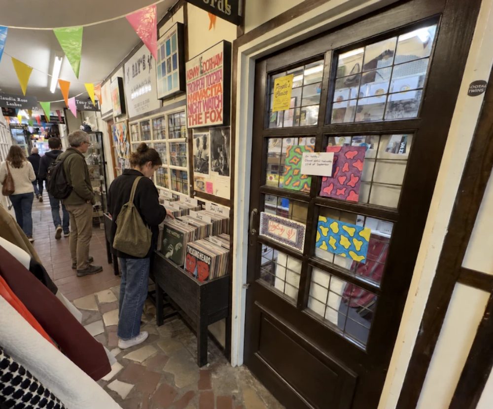 The Antique City aisle, a shopper flicking through record racks under bunting, with unit signs hanging down the corridor