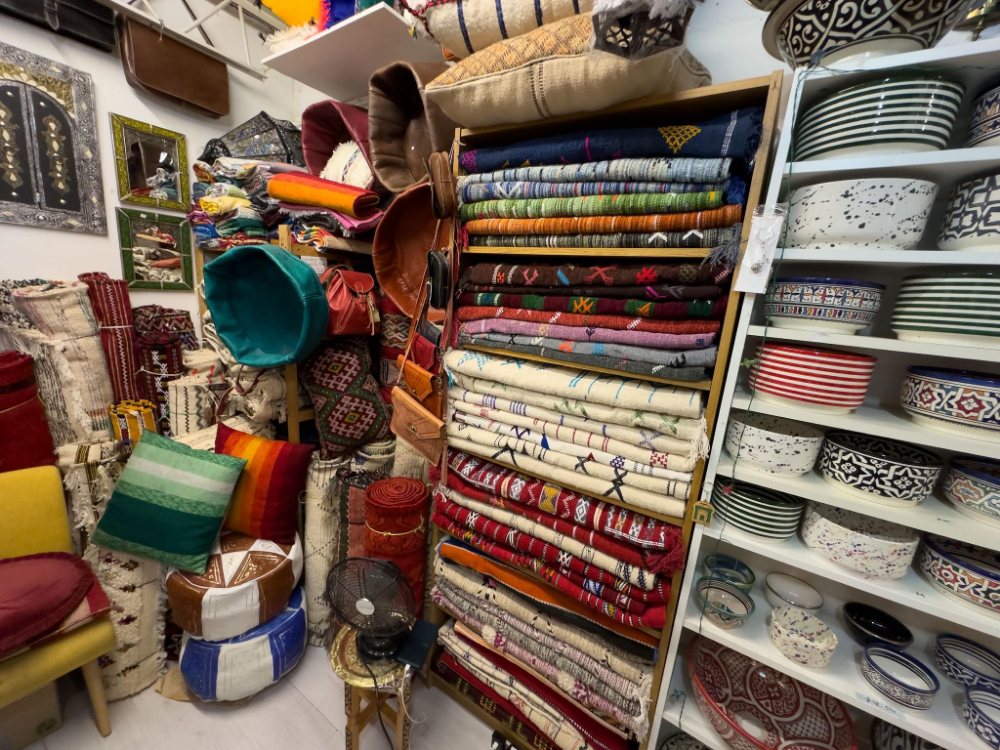 Inside Moroccan Corner: stacked rugs, leather bags, poufs and painted ceramics