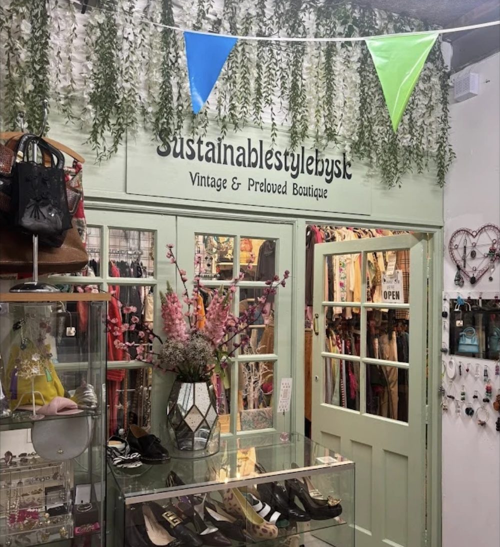 Sustainable style by S&K, a sage green shopfront signed Vintage and Preloved Boutique under trailing foliage, rails of clothes inside and shoes in the glass case
