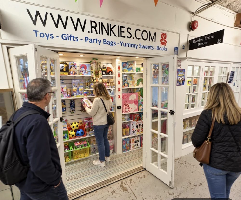Rinkies Toys, open double doors under a sign listing toys, gifts, party bags and sweets, the shelves inside stacked with games and soft toys