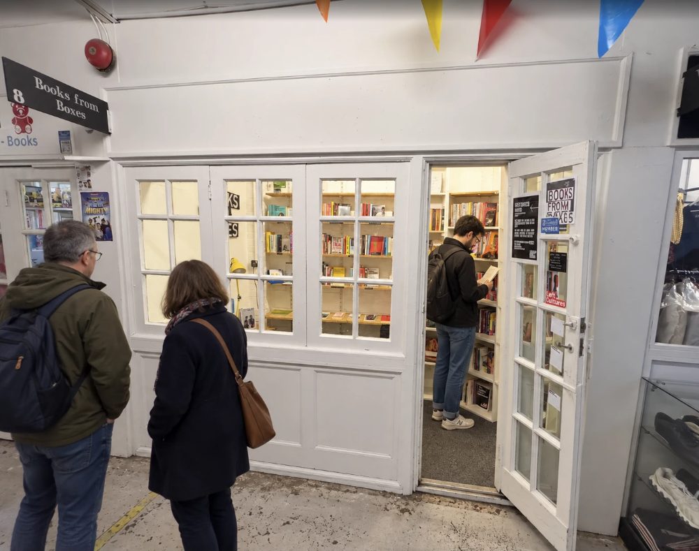 Books From Boxes at unit 8, a white glazed shopfront with the door open onto shelves of books and a customer reading inside